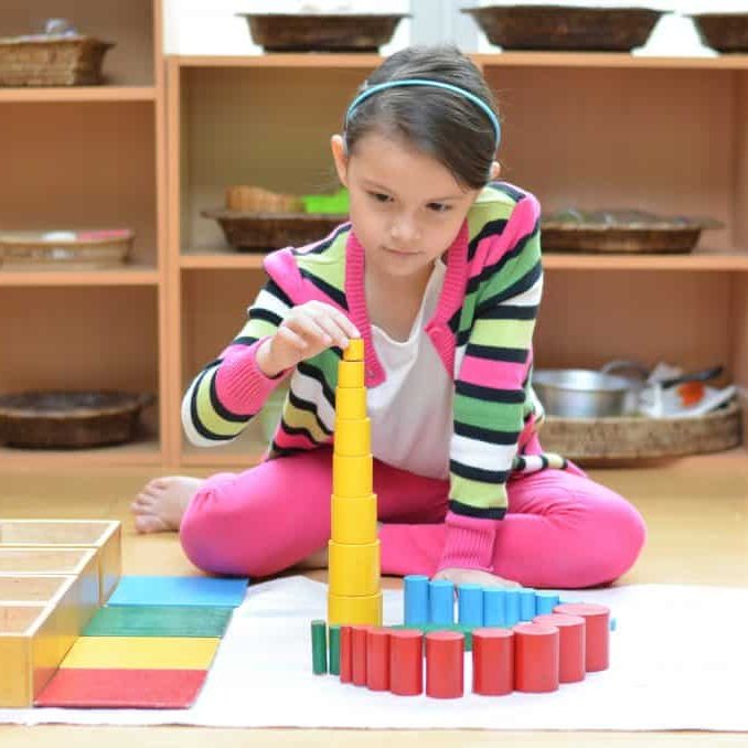 Little girl hand building tower made of montessori educational materials